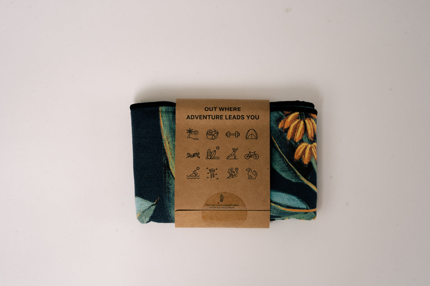 Folded Outwhere PH Everywhere Towel in Saging (banana) Green in Packaging sleeve. Back of packaging sleeve shows tag line OUT WHERE ADVENTURE LEADS YOU, and icons that show different activities to use the towel with.