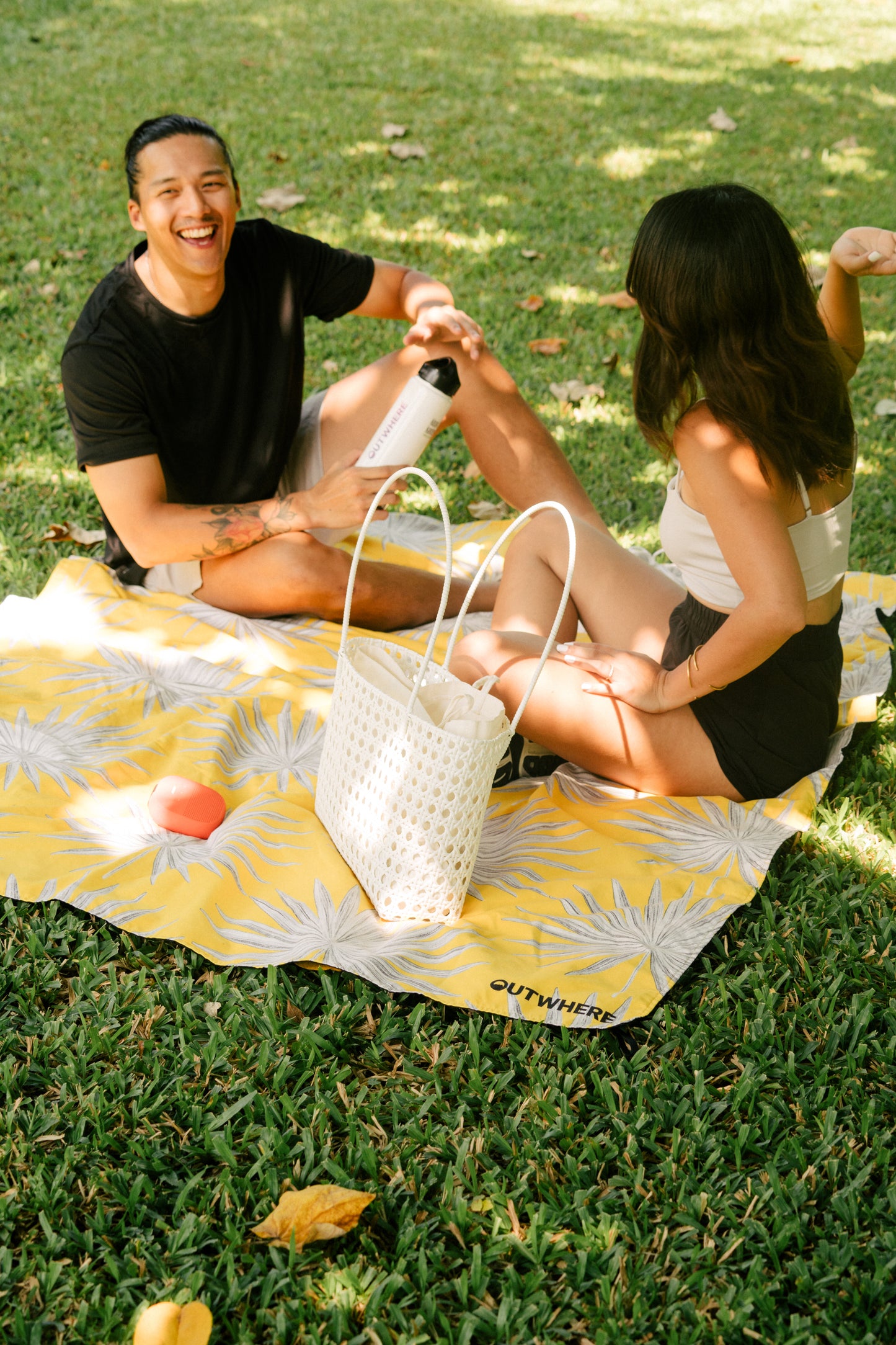 Couple sitting on the Outwhere PH Latag mat in Anahaw on the grass having a picnic