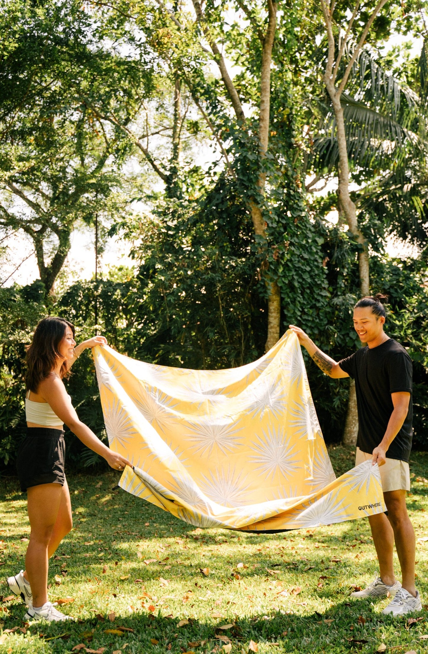 Couple holding out the ends of the Outwhere PH Latag mat in Anahaw about to lay it on the grass in the park