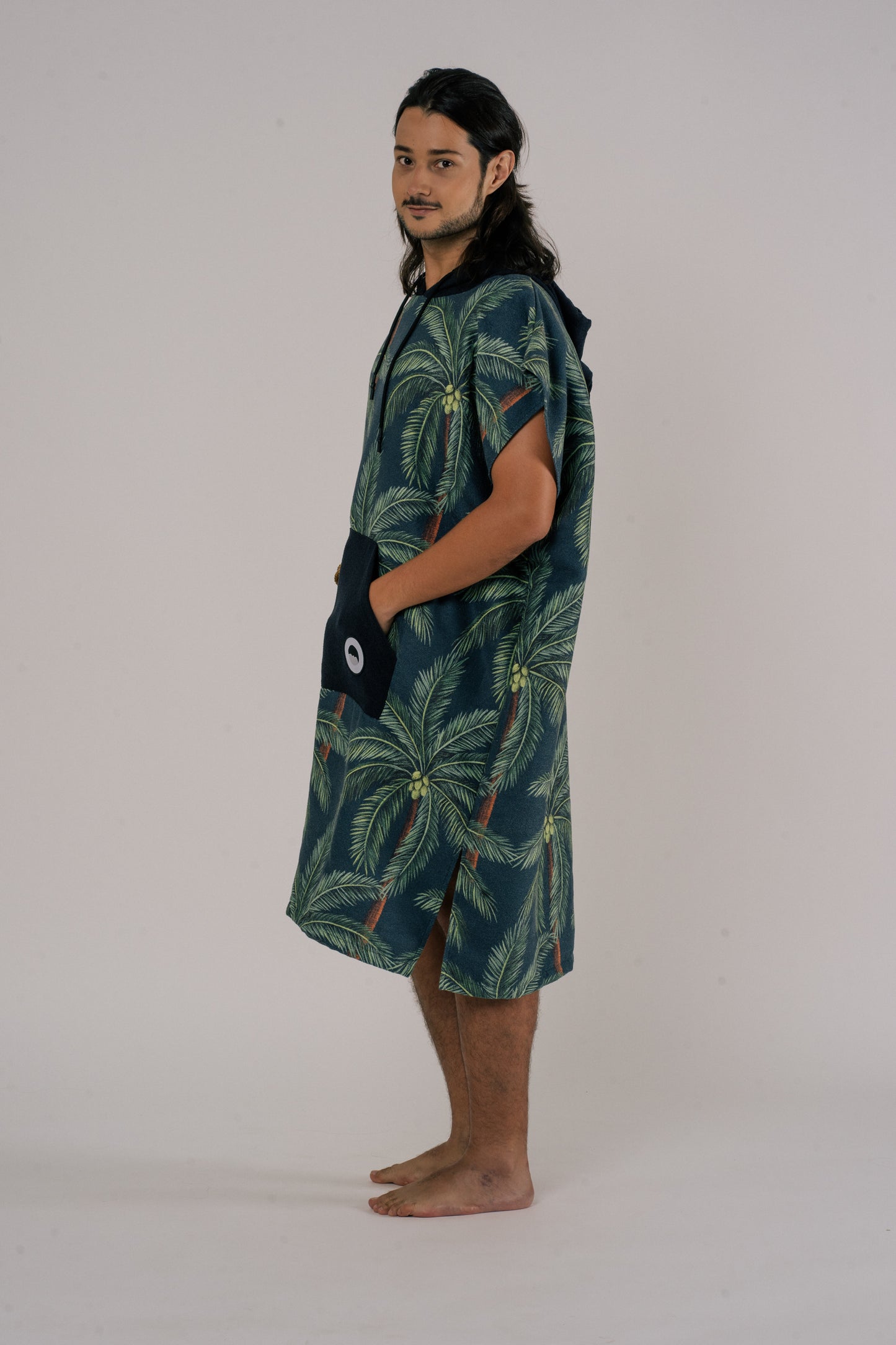 Male model wearing Outwhere Changing Poncho Towel in Buko design, Coconut tree print standing sideview