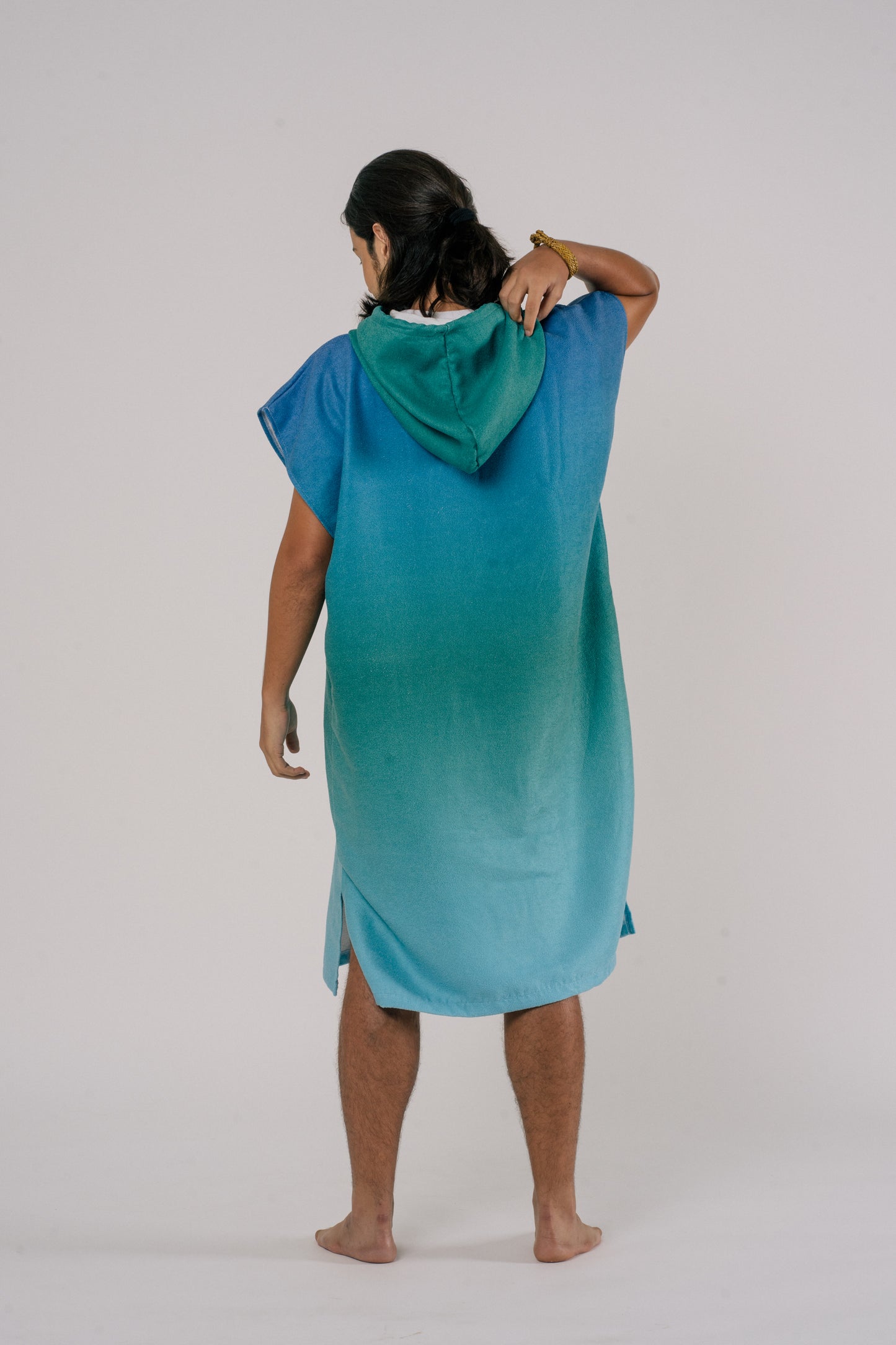 male wearing Outwhere Changing Poncho Towel in Dagat (ocean) design, showing back side of poncho, shades of blue and green