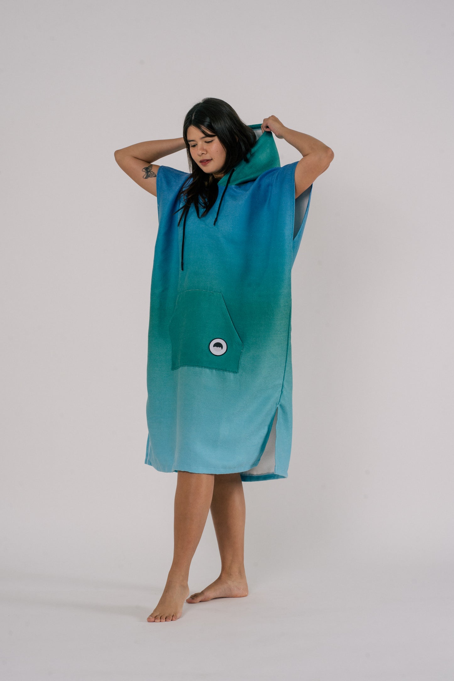 Female wearing Outwhere Changing Poncho Towel in Dagat (ocean) design, shades of blue and green, holding hood