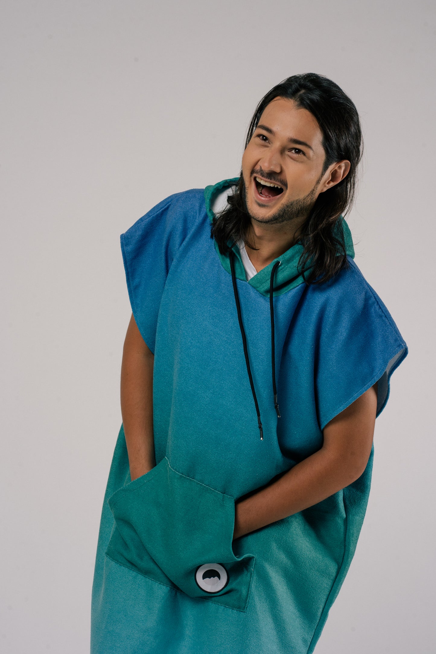 Male wearing Outwhere Changing Poncho Towel in Dagat (ocean) design, shades of blue and green, hands in pocket