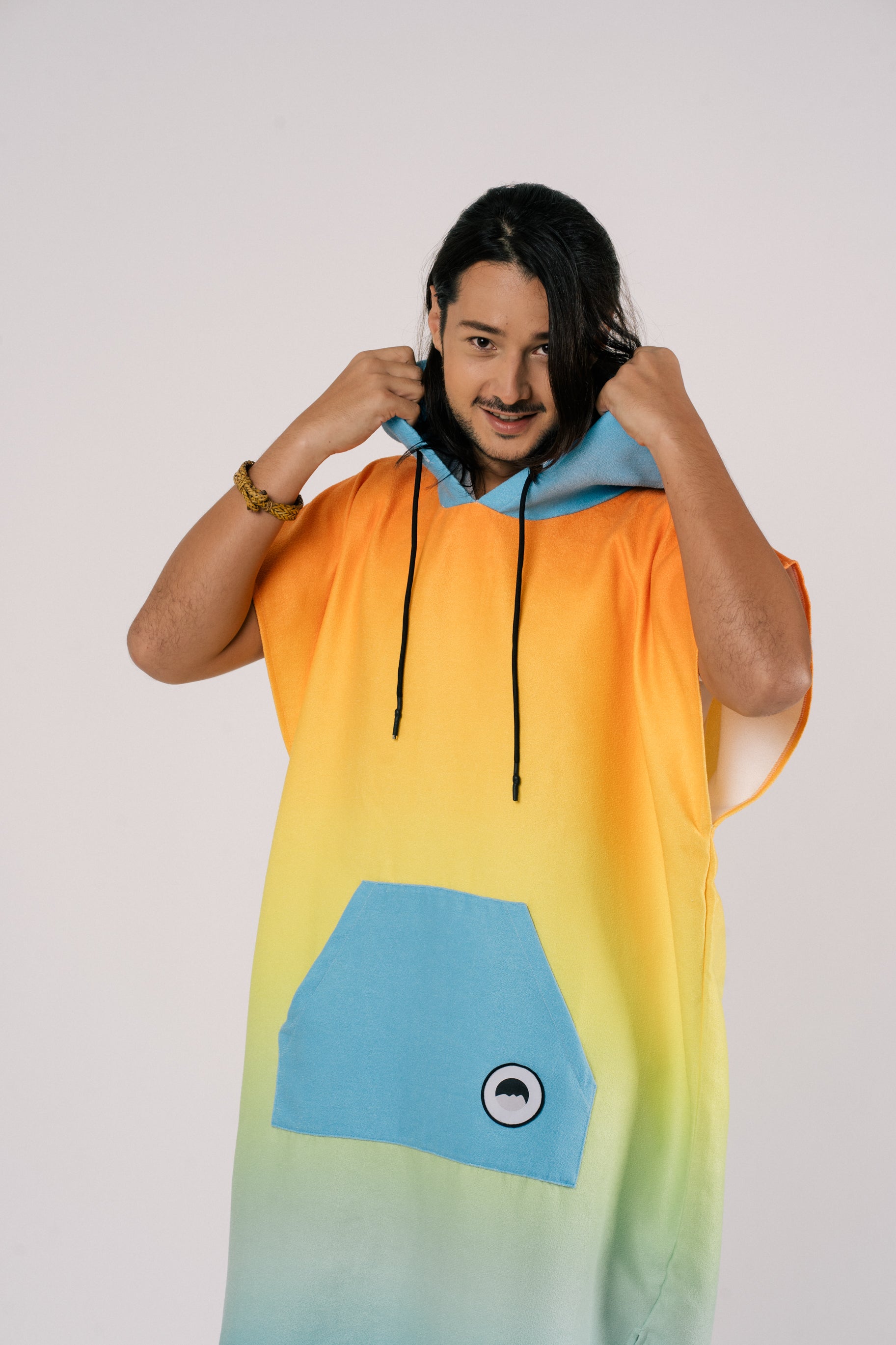 Male wearing Outwhere Changing Poncho Towel in Liwayway (dawn) design, gradient shades of orange, turquoise, yellow, green