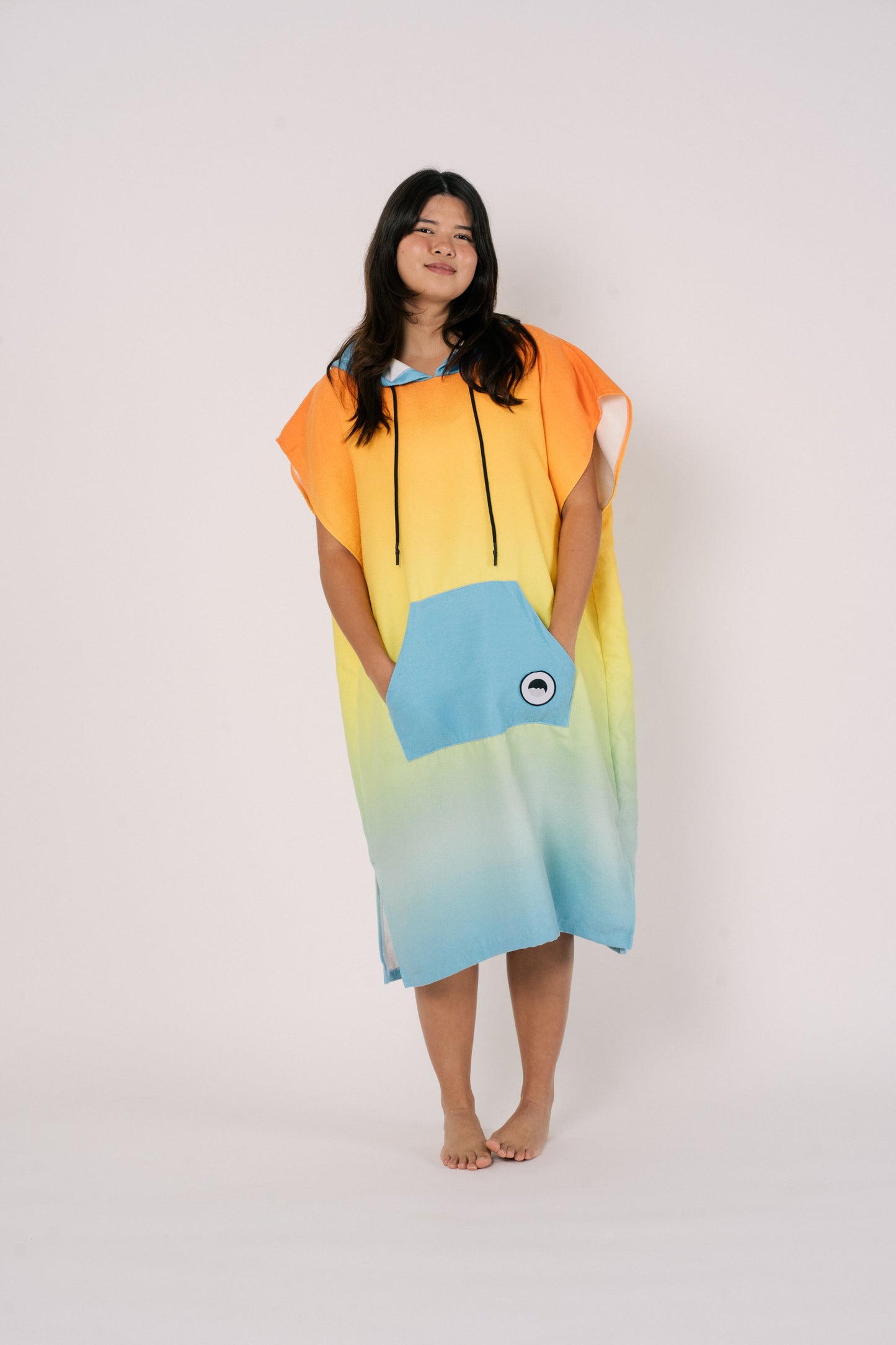 Female wearing Outwhere Changing Poncho Towel in Liwayway (dawn) design, gradient shades of orange, turquoise, yellow, green