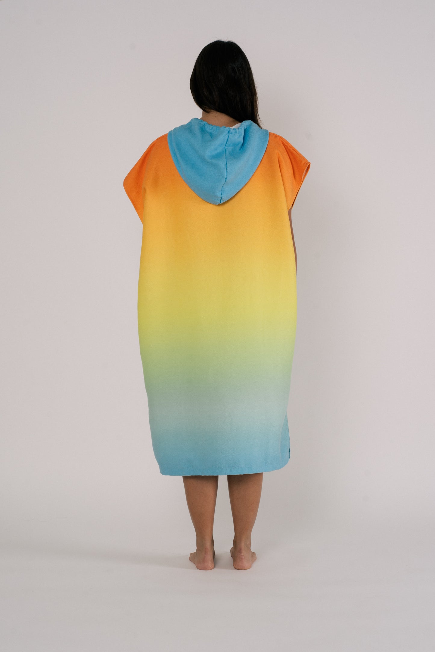 Female showing back design of Outwhere Changing Poncho Towel in Liwayway (dawn) design, gradient shades of orange, turquoise, yellow, green