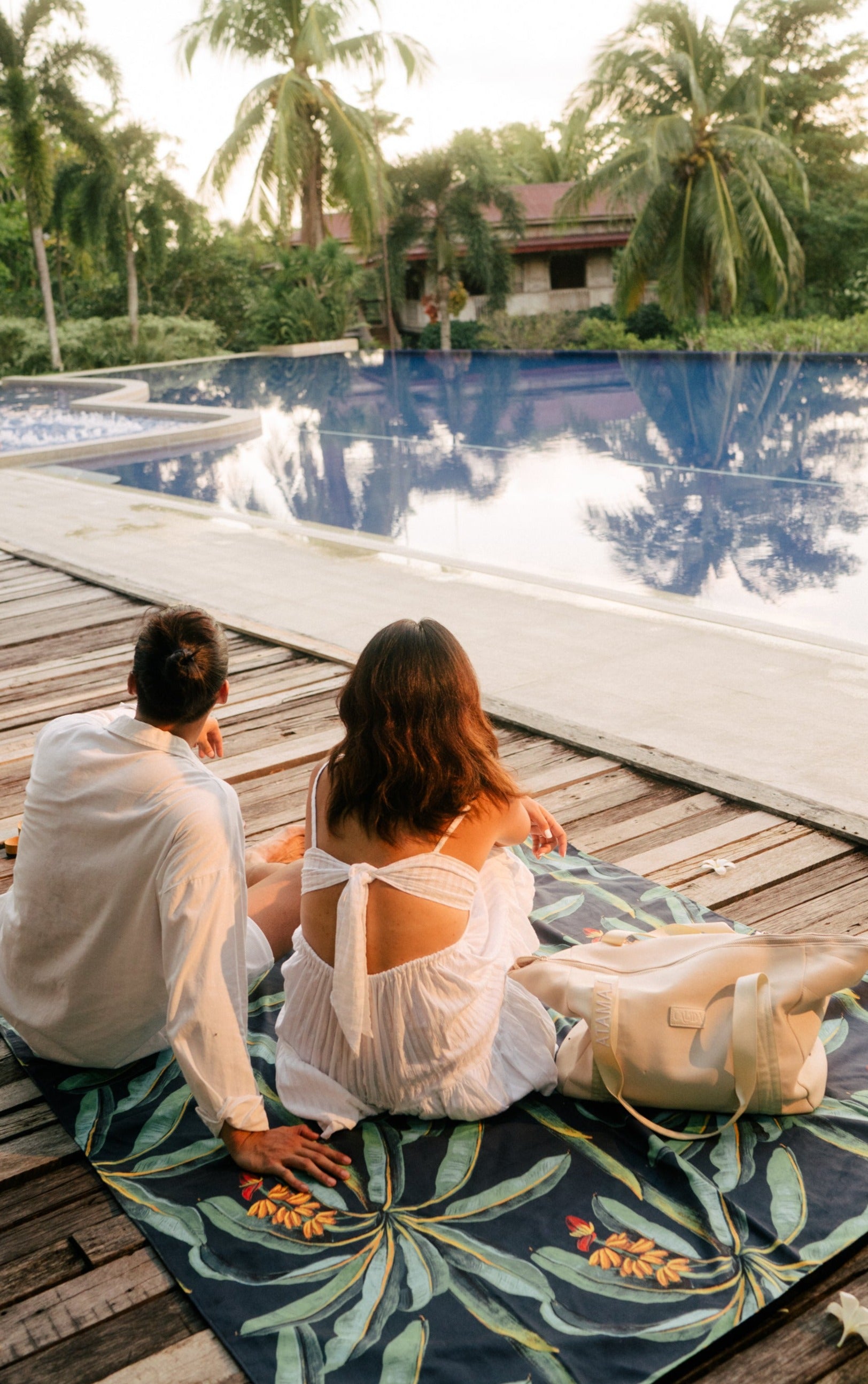Back view of a couple sitting on the Outwhere PH Latag mat in Saging facing a pool with trees in the background